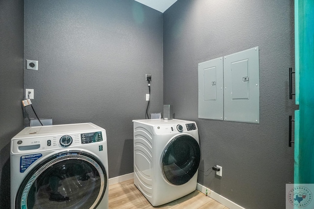 clothes washing area with electric panel, light hardwood / wood-style floors, and washing machine and clothes dryer