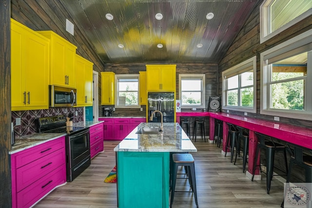 kitchen featuring black appliances, lofted ceiling, sink, a kitchen breakfast bar, and a center island with sink