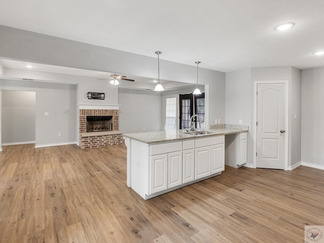 kitchen with light stone counters, open floor plan, hanging light fixtures, white cabinetry, and a sink