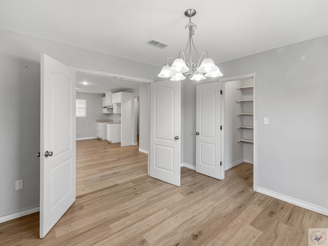 unfurnished dining area with light wood-type flooring, an inviting chandelier, baseboards, and visible vents