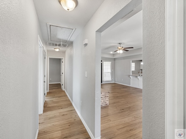 hallway with attic access, baseboards, visible vents, and light wood finished floors