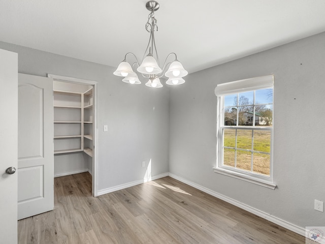 unfurnished dining area with a notable chandelier, light wood-type flooring, and baseboards