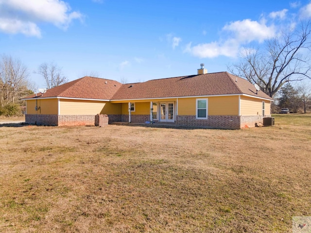 rear view of property featuring french doors, brick siding, a chimney, a lawn, and central AC