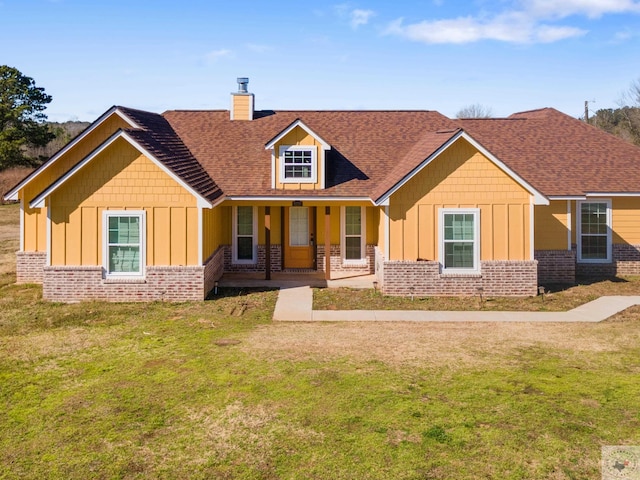 view of front facade with a porch, brick siding, a front lawn, board and batten siding, and a chimney