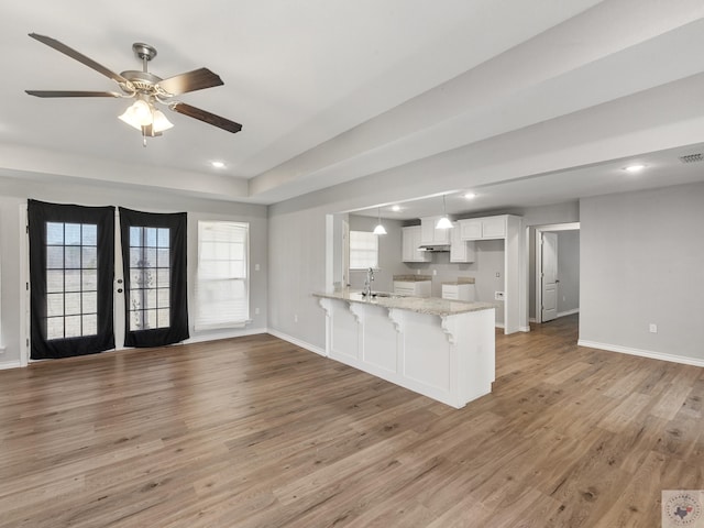 kitchen with a breakfast bar area, a peninsula, a sink, white cabinets, and open floor plan