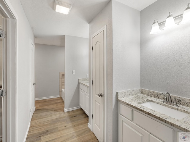 bathroom featuring baseboards, a bathtub, wood finished floors, and vanity