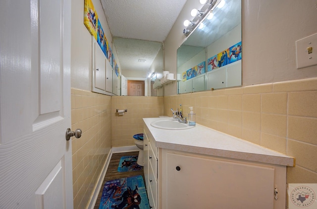 bathroom featuring toilet, a textured ceiling, vanity, and tile walls