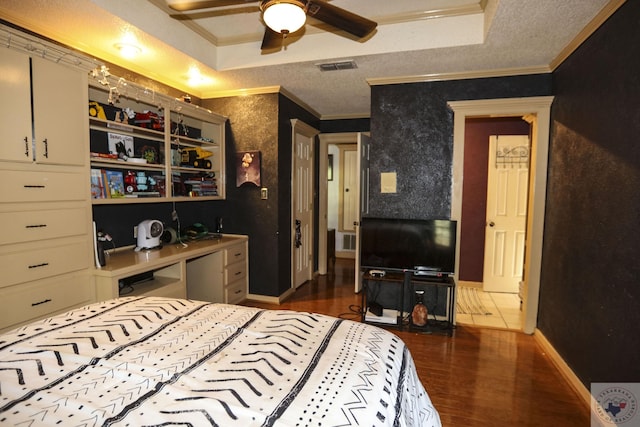 bedroom with a textured ceiling, a raised ceiling, ornamental molding, dark wood-type flooring, and ceiling fan