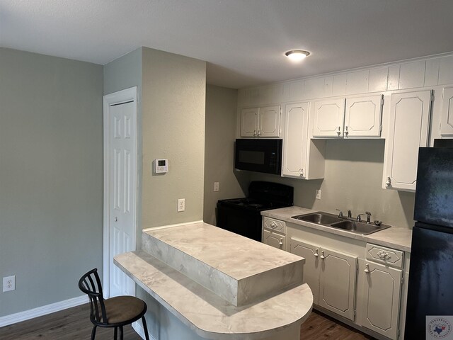 kitchen with kitchen peninsula, dark hardwood / wood-style flooring, sink, white cabinets, and black appliances