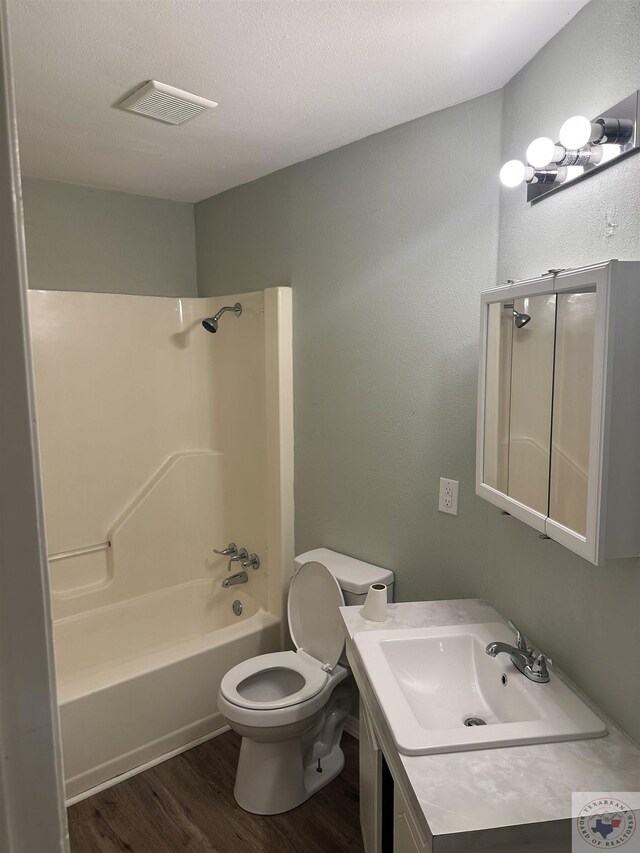 full bathroom featuring shower / washtub combination, hardwood / wood-style floors, toilet, a textured ceiling, and vanity