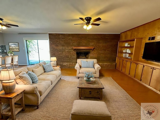 living room featuring brick wall, light wood-type flooring, ceiling fan, and a brick fireplace