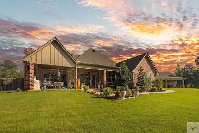 back house at dusk with a patio area and a lawn