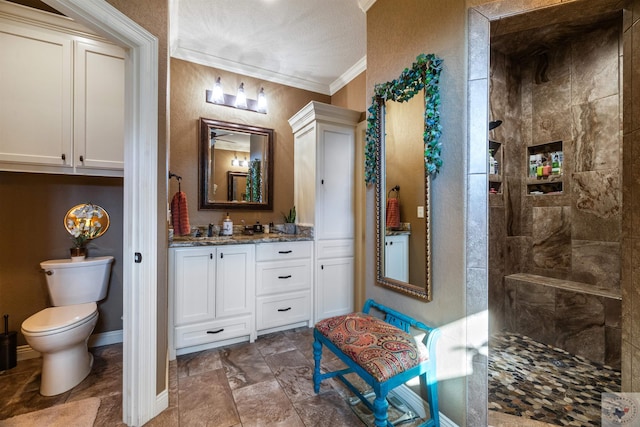 bathroom featuring a tile shower, toilet, vanity, and ornamental molding