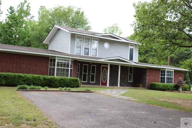 traditional-style house featuring covered porch, a front lawn, and brick siding