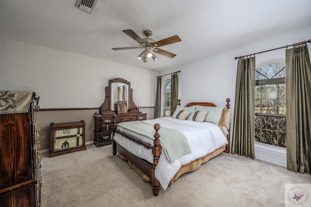 bedroom featuring visible vents, light colored carpet, a ceiling fan, and a textured ceiling