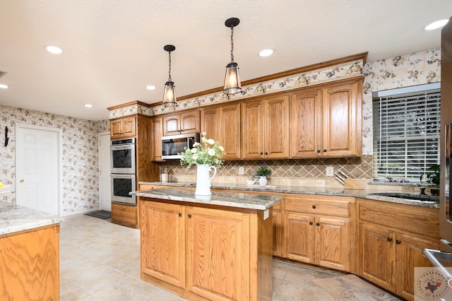 kitchen with pendant lighting, light stone counters, a center island, appliances with stainless steel finishes, and wallpapered walls