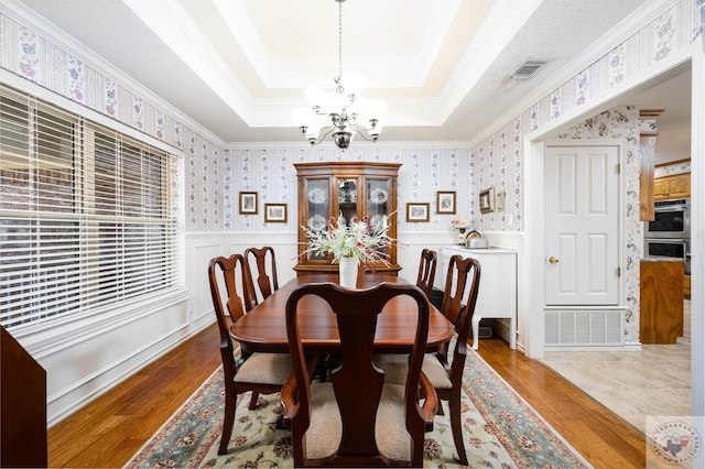 dining room with a wainscoted wall, a raised ceiling, visible vents, and wallpapered walls