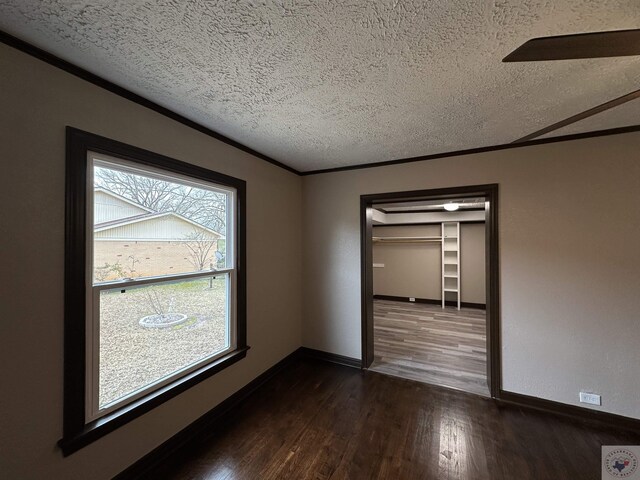 empty room featuring crown molding, plenty of natural light, a textured ceiling, and dark hardwood / wood-style flooring