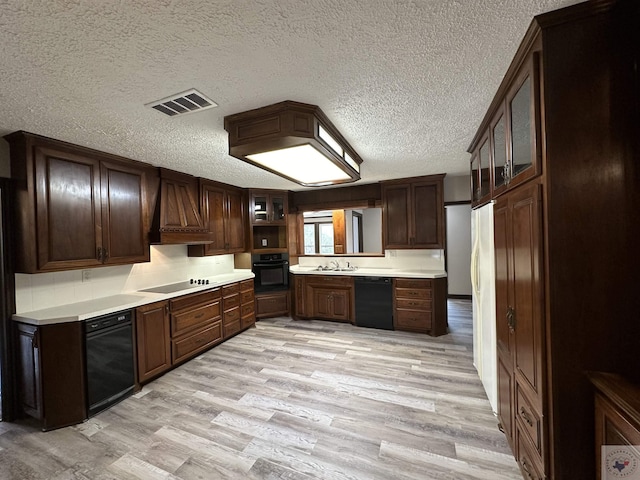 kitchen with black appliances, a textured ceiling, custom range hood, light wood-type flooring, and dark brown cabinets