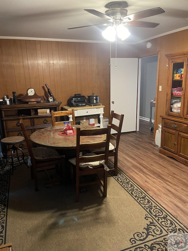 dining room featuring crown molding, wooden walls, and ceiling fan