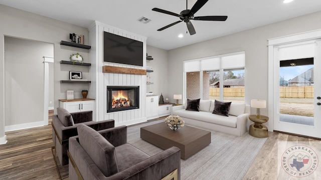 living room with a large fireplace, ceiling fan, and wood-type flooring