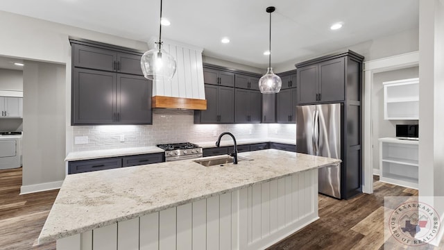 kitchen with light stone countertops, stainless steel appliances, an island with sink, sink, and hanging light fixtures