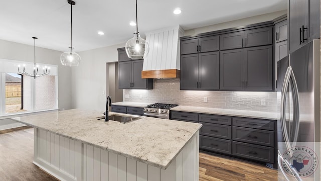 kitchen with pendant lighting, appliances with stainless steel finishes, custom exhaust hood, an island with sink, and sink