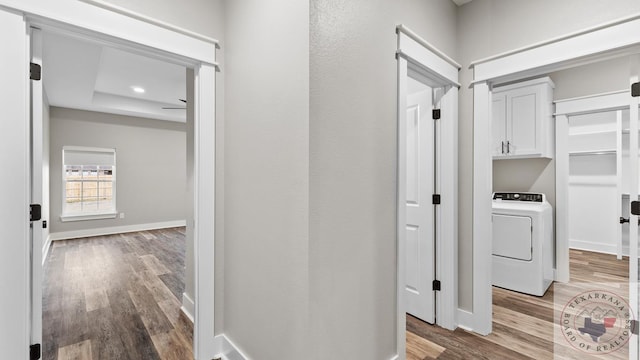 corridor featuring washer / clothes dryer, light wood-type flooring, and a raised ceiling