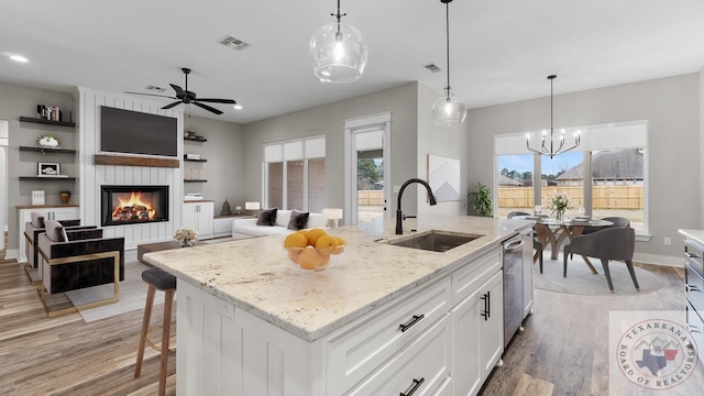 kitchen with hanging light fixtures, sink, white cabinets, light stone counters, and a kitchen island with sink