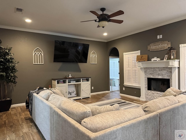 living room featuring crown molding, hardwood / wood-style floors, ceiling fan, and a stone fireplace