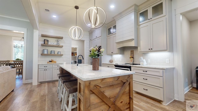 kitchen featuring light stone countertops, backsplash, hanging light fixtures, a kitchen island with sink, and crown molding