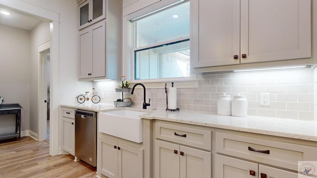 kitchen with light stone countertops, tasteful backsplash, dishwasher, sink, and light wood-type flooring