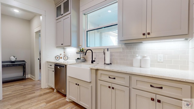 kitchen with dishwasher, sink, backsplash, light wood-type flooring, and light stone counters