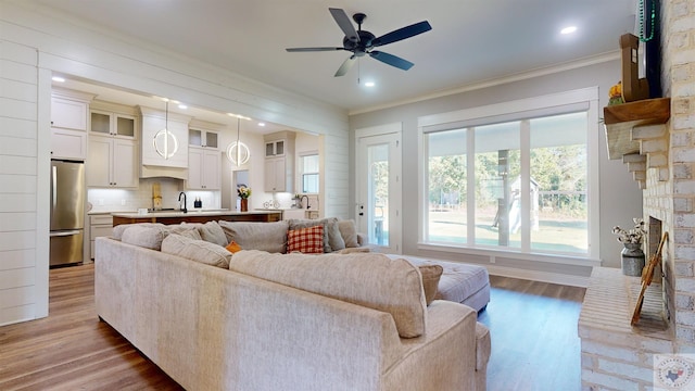 living room featuring light wood-type flooring, ceiling fan, a brick fireplace, and crown molding