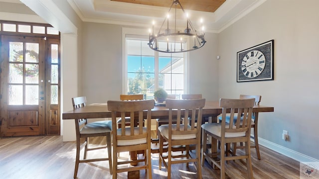 dining room featuring wood-type flooring, a tray ceiling, a notable chandelier, and crown molding