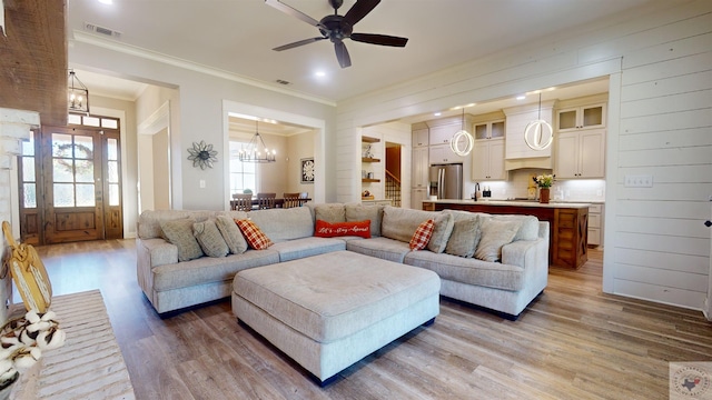 living room with wood-type flooring, ceiling fan with notable chandelier, a wealth of natural light, and crown molding