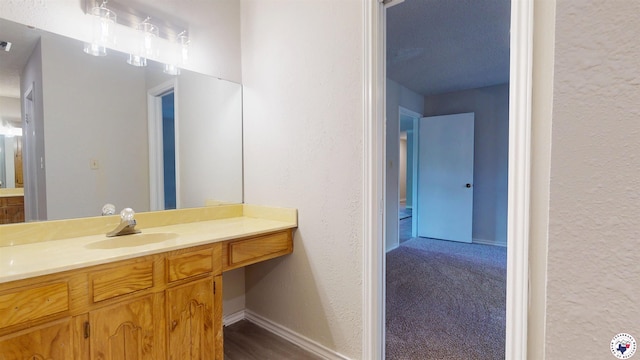 bathroom with visible vents, a textured wall, baseboards, and vanity