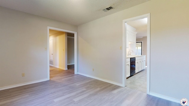 spare room featuring visible vents, baseboards, a sink, light wood-style floors, and a textured ceiling