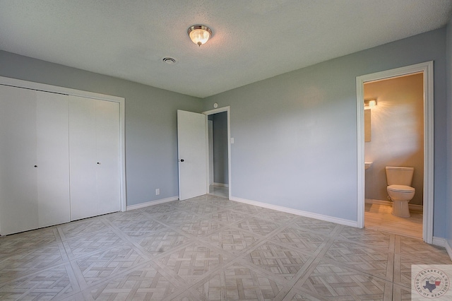 unfurnished bedroom with a textured ceiling, a closet, and ensuite bath