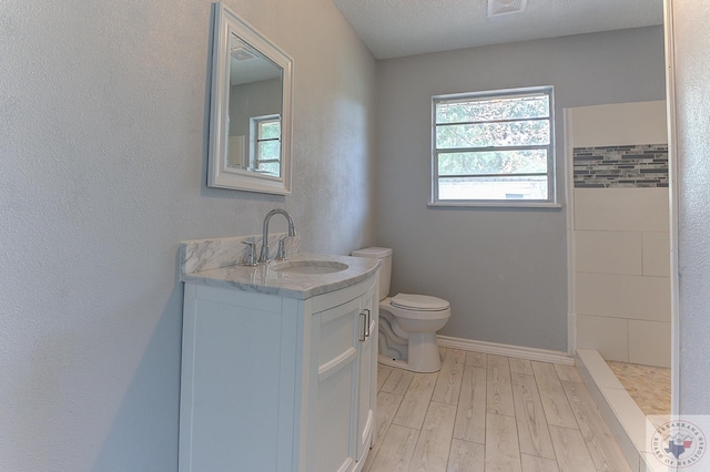 bathroom featuring a textured ceiling, wood-type flooring, vanity, toilet, and a tile shower