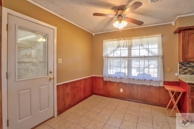 unfurnished dining area with crown molding, visible vents, wainscoting, wooden walls, and a textured ceiling