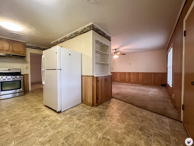 kitchen featuring ceiling fan, gas stove, a wainscoted wall, freestanding refrigerator, and under cabinet range hood