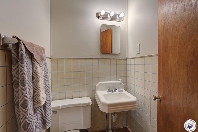half bath with a sink, wainscoting, toilet, and tile walls