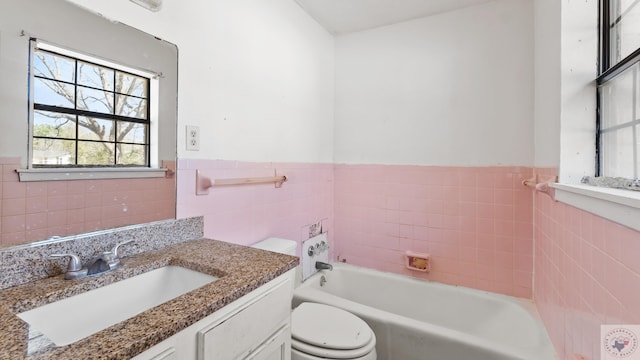 bathroom featuring tile walls, a wainscoted wall, toilet, a bathing tub, and vanity