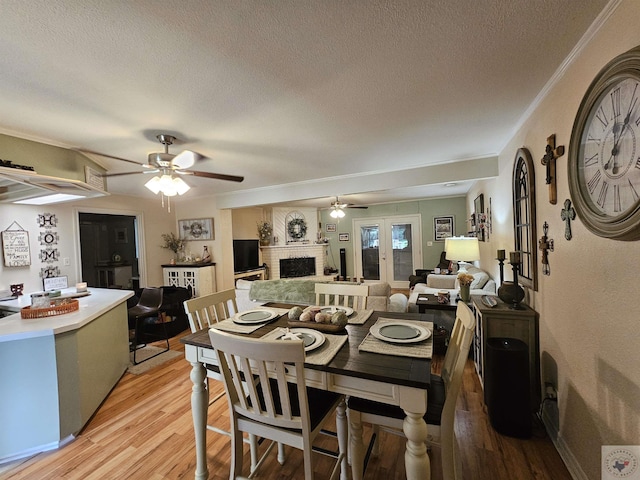 dining room featuring hardwood / wood-style floors, a textured ceiling, a brick fireplace, french doors, and ceiling fan