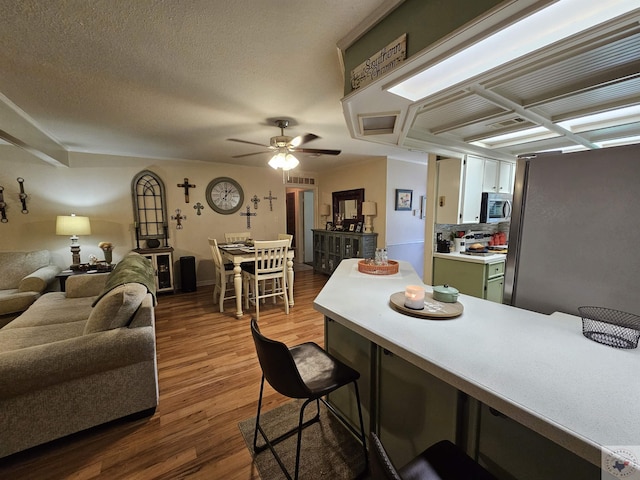 kitchen featuring ceiling fan, appliances with stainless steel finishes, hardwood / wood-style floors, a textured ceiling, and green cabinetry