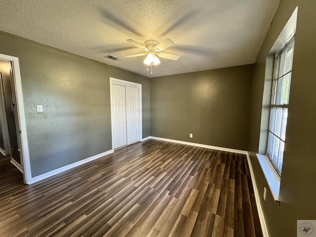 unfurnished bedroom with dark wood-type flooring, a textured ceiling, a closet, and ceiling fan