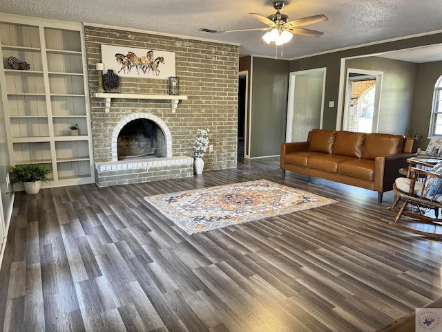 living room featuring a fireplace, a textured ceiling, ornamental molding, dark wood-type flooring, and ceiling fan