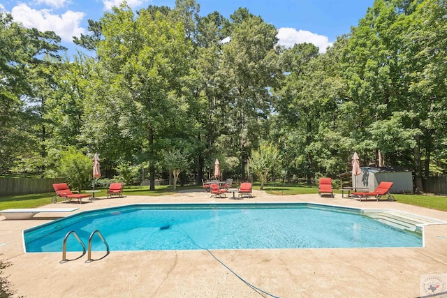 view of pool with a diving board, a patio area, and a storage shed