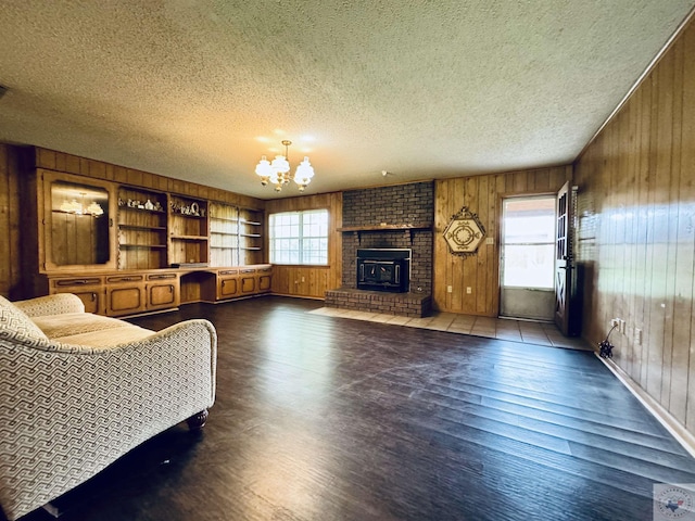 living room with a textured ceiling, a brick fireplace, an inviting chandelier, built in features, and wood walls